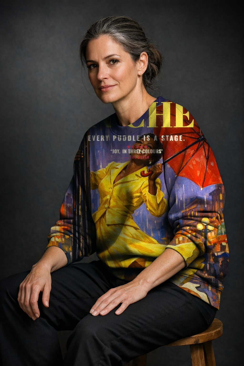 A woman seated on a stool in a sweatshirt printed edge to edge with the Technicolor Musical poster of Imani, one hard light